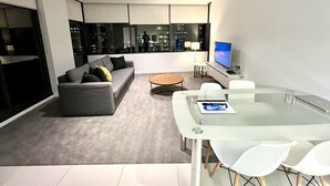A modern living room with a sofa, coffee table, and glass-top dining table. - Stunning City View 2BR in CBD by Readyset Apartments (Melbourne)
