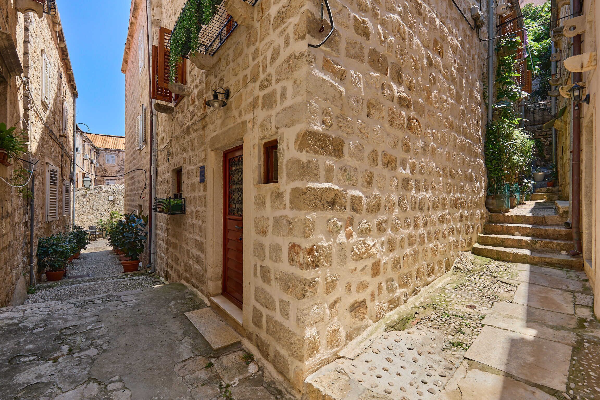 A narrow stone street with a building featuring a wooden door and potted plants.