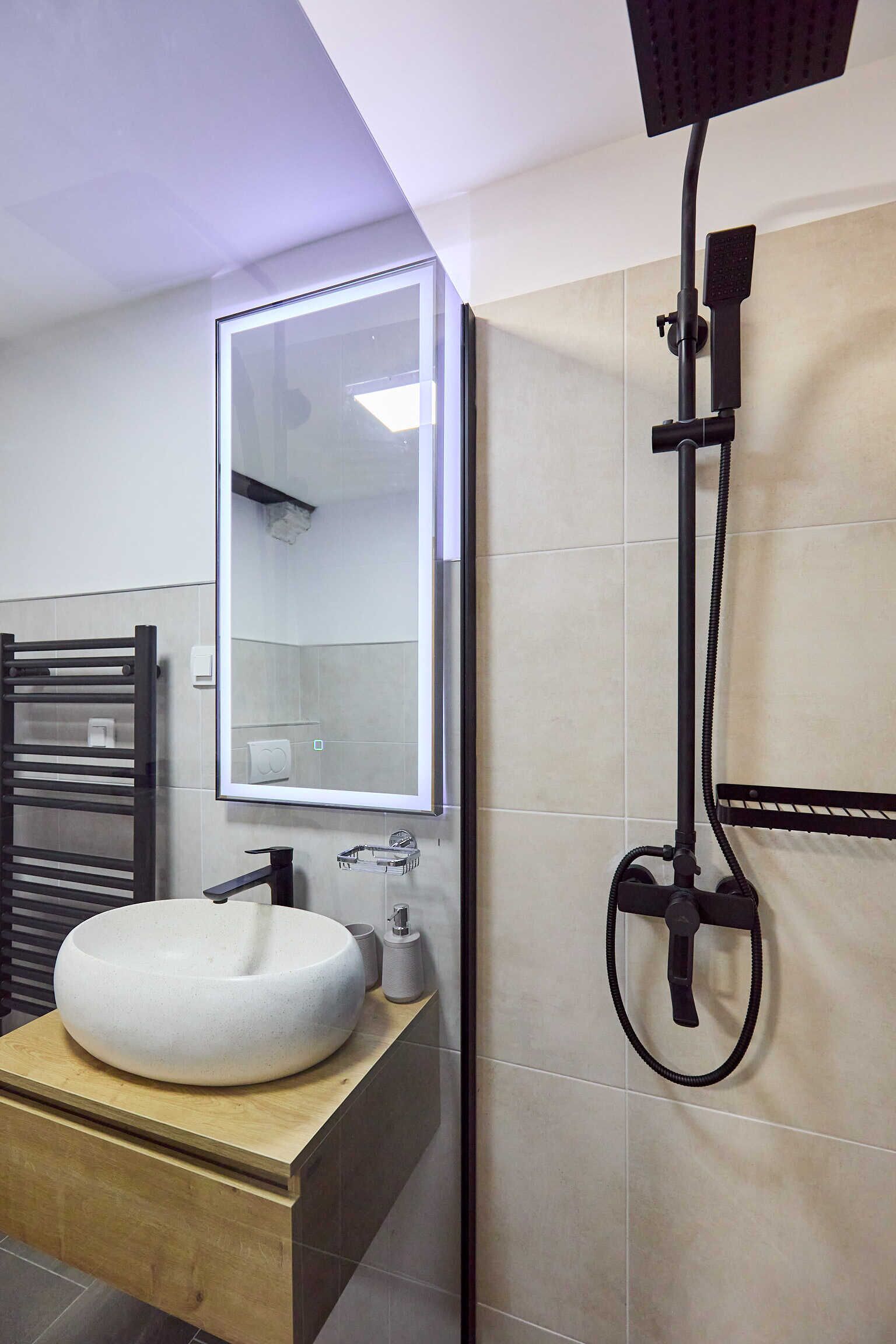 Un baño moderno con un espejo grande, un lavamanos redondo y una ducha.