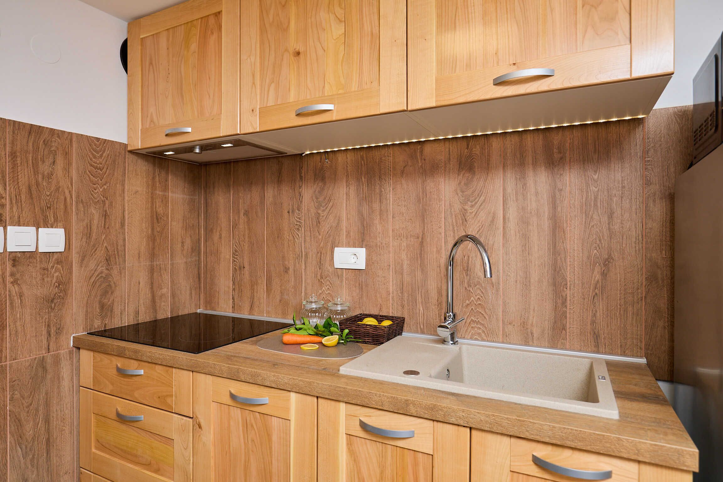 A modern kitchen with wooden cabinetry, a black induction cooktop, a stainless steel sink, and a built-in range hood.