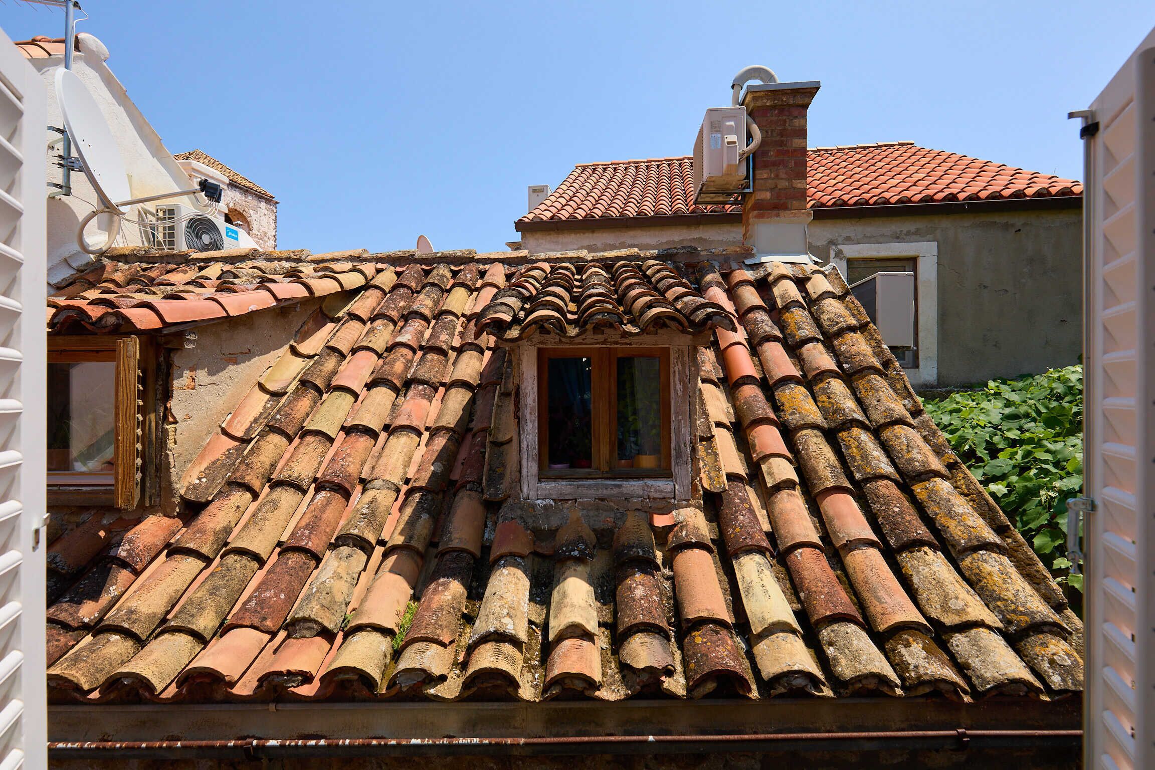 Un bâtiment avec un toit recouvert de tuiles, une petite fenêtre et une antenne parabolique.