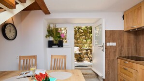 A kitchen with wooden cabinets, a dining table with chairs, a clock, and a view of the garden through an open door. - Hedera Estate, Hedera A6 (Dubrovnik)