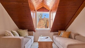 A cozy attic room with a sloped wooden ceiling, two beige sofas, a wooden coffee table, and a window with a view of a tiled roof. - Hedera Estate, Hedera A6 (Dubrovnik)