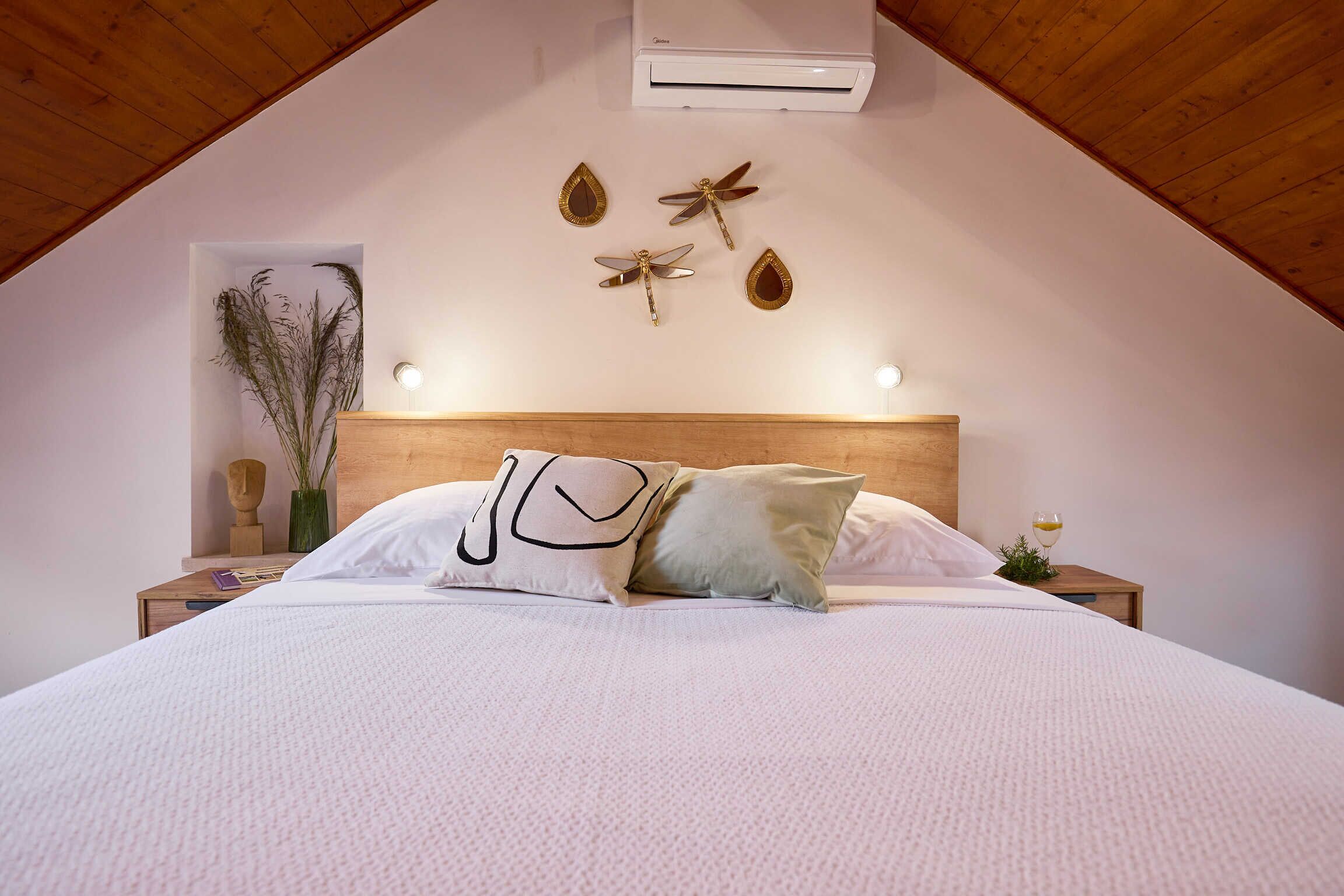 A bedroom with a sloped ceiling, a wooden headboard, a bed with white bedding, decorative dragonfly wall art, and a bedside table with a glass of water.