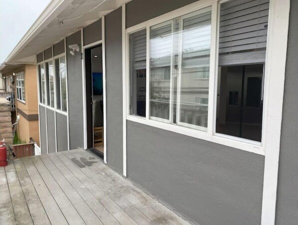 Een woongebouw met een grijze gevel, witte raamkozijnen en een houten terras.