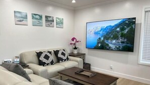 Een moderne woonkamer met een beige bank, een salontafel en een grote flatscreen televisie aan de muur.