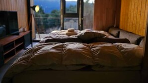 Un dormitorio con una cama grande, un televisor sobre un soporte de madera y vistas a montañas a través de un ventanal.