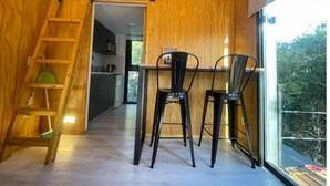 Cocina compacta con detalles de madera, comedor con dos sillas y un tragaluz sobre la mesa.
