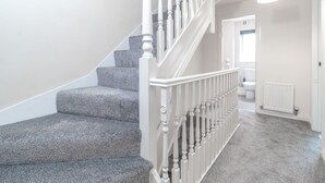 A staircase with white balusters leading to a landing, carpeted steps, and a white radiator on the wall. - Westlake Serviced Accommodation  (Peterborough)