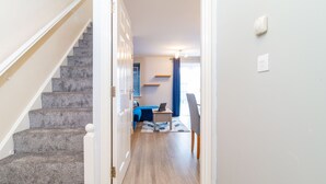 A hallway with carpeted stairs leading to a room with a bed, a chair, and a desk. - Westlake Serviced Accommodation  (Peterborough)