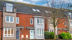 A row of two-story townhouses with brick facades, white-framed windows, and a tree in the foreground. - Westlake Serviced Accommodation  (Peterborough)