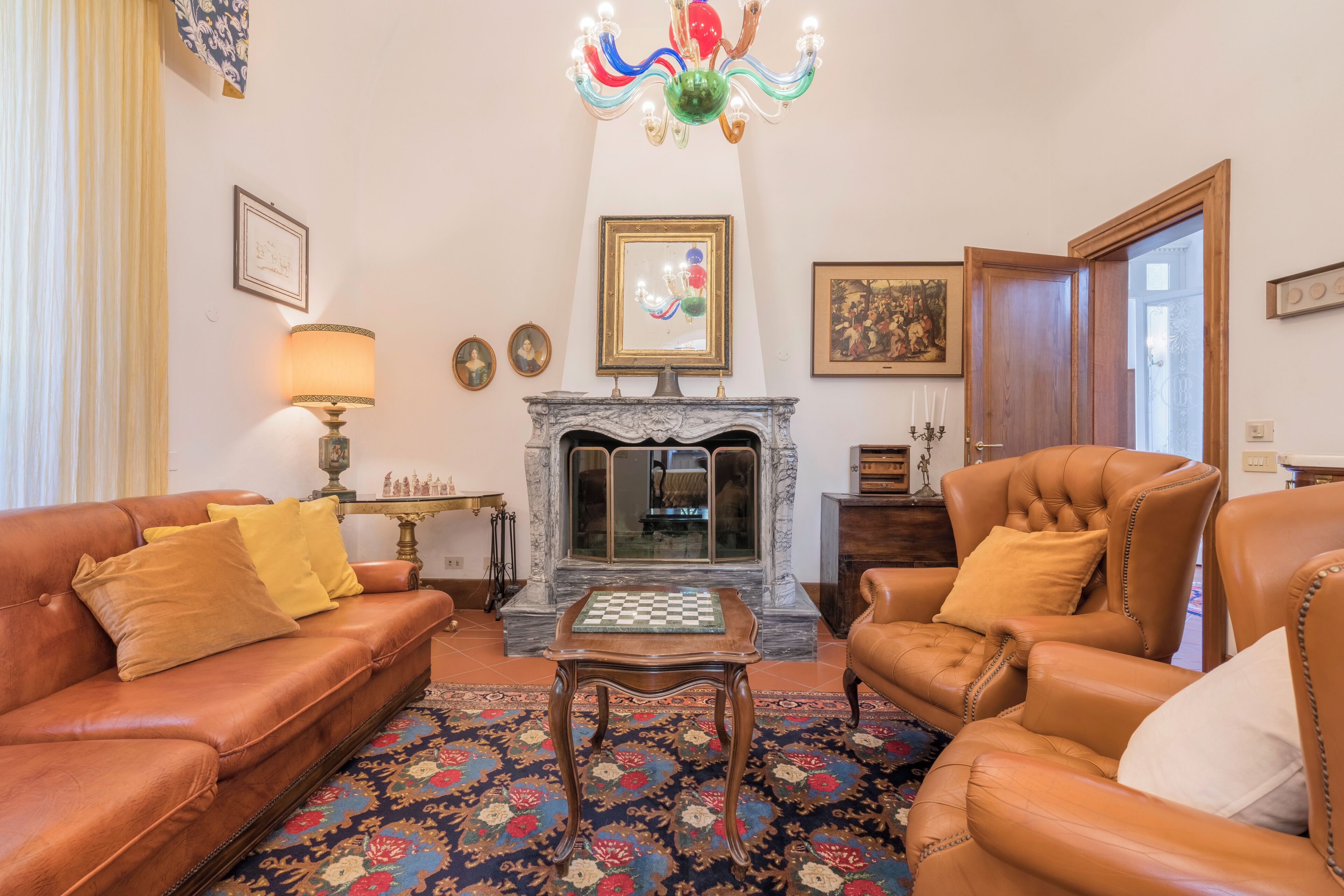 A living room with a fireplace, leather sofas, a chess table, and a chandelier.