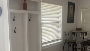 A white built-in bench with hooks, a small table with chairs, and a window with blinds. - Charming home with Oak Tree lined streets in the heart of Lake Charles. (Lake Charles)