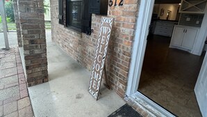 A brick exterior with a welcome sign, a number '512' sign, and a door leading to a kitchen area. - Charming home with Oak Tree lined streets in the heart of Lake Charles. (Lake Charles)