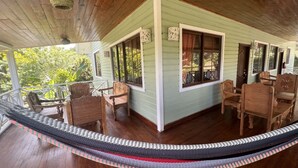 Une véranda couverte avec des chaises en bois et un tapis tissé.