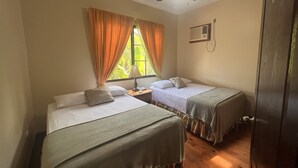 Une chambre avec deux lits simples, une table de chevet, une lampe et une fenêtre avec des rideaux.