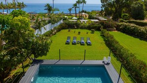 A pool with lounge chairs, a view of the ocean, and a well-maintained lawn.