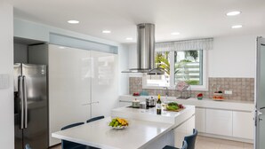 A modern kitchen with a central island, white cabinetry, stainless steel appliances, and blue chairs.