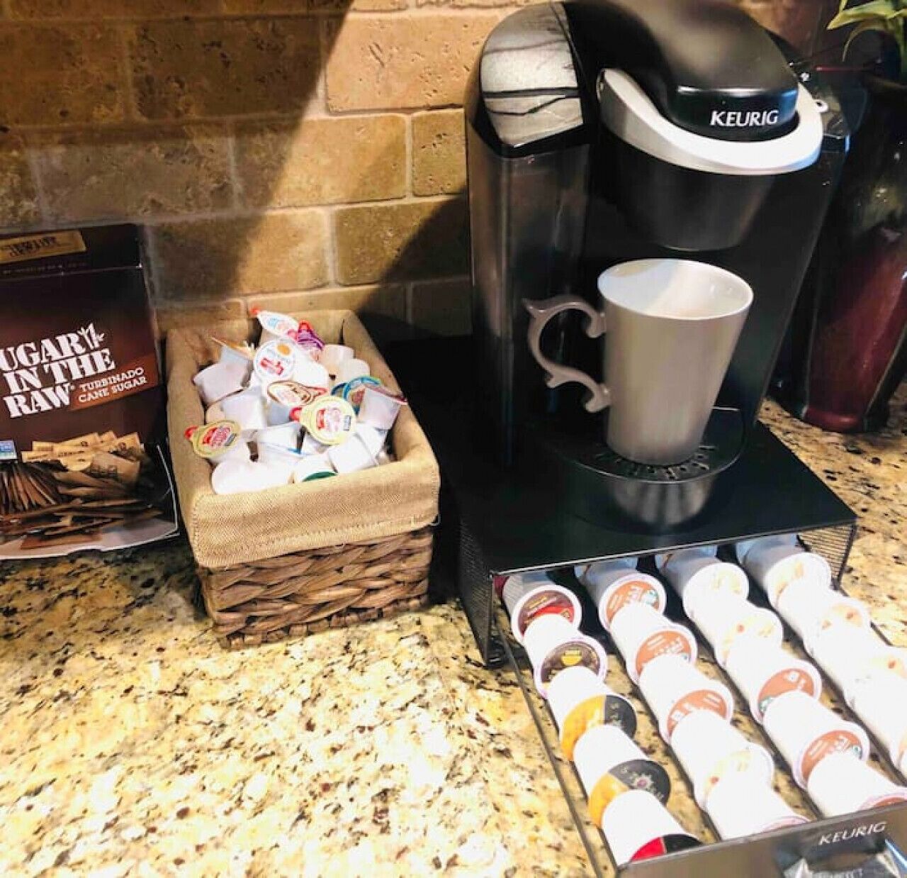 A Keurig coffee machine with a cup holder, a basket of sugar packets, and a display of coffee pods.