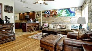 Un salón amplio con suelo de madera, un sofá de cuero, una mesa de centro y una zona de comedor con armarios de madera y una barra.