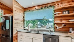 Uma cozinha moderna com paredes de madeira, uma geladeira de aço inoxidável, uma lava-louças e uma janela com vista para o exterior.