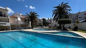 Une piscine à l’eau d’un bleu cristallin, entourée de bâtiments blancs dotés de balcons et de palmiers.