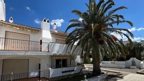 Un bâtiment à deux étages avec une façade blanche, un balcon et un palmier au premier plan.