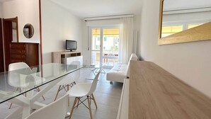 A modern living room with a glass dining table, white chairs, a wooden sideboard, a television, and a large mirror. - AED Home   (Lavagna)