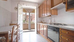 A kitchen with wooden cabinets, a stove, and a dining area with a table and chairs. - AED Home   (Lavagna)