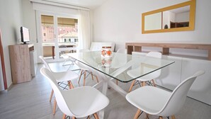 A modern dining area with a glass table and white chairs, a wooden cabinet, and a large mirror on the wall. - AED Home   (Lavagna)