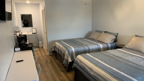 A compact hotel room with two single beds, a small desk with a chair, a coffee machine, and a mirror. - Double Queen Room (Warsaw)