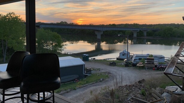 A covered outdoor area with a view of a sunset over a river and a bridge. - Double Queen Room (Warsaw)