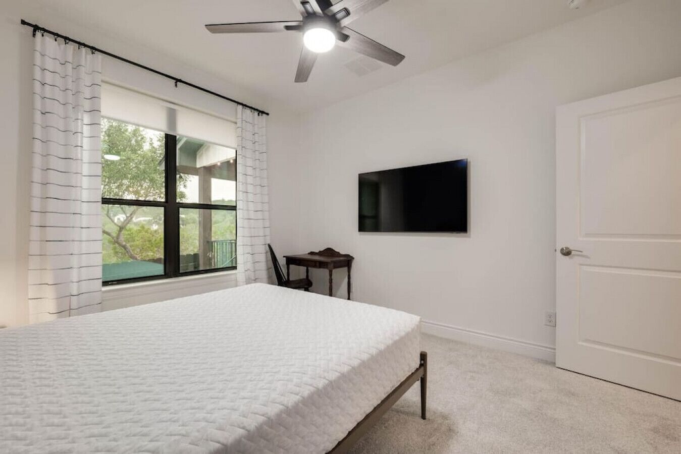 A bedroom with a bed, a desk, a chair, a TV, and a ceiling fan.