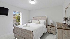Ein Schlafzimmer mit einem hölzernen Bett, weißer Bettwäsche, einem Nachttisch mit Lampe und einem an der Wand montierten Fernseher.