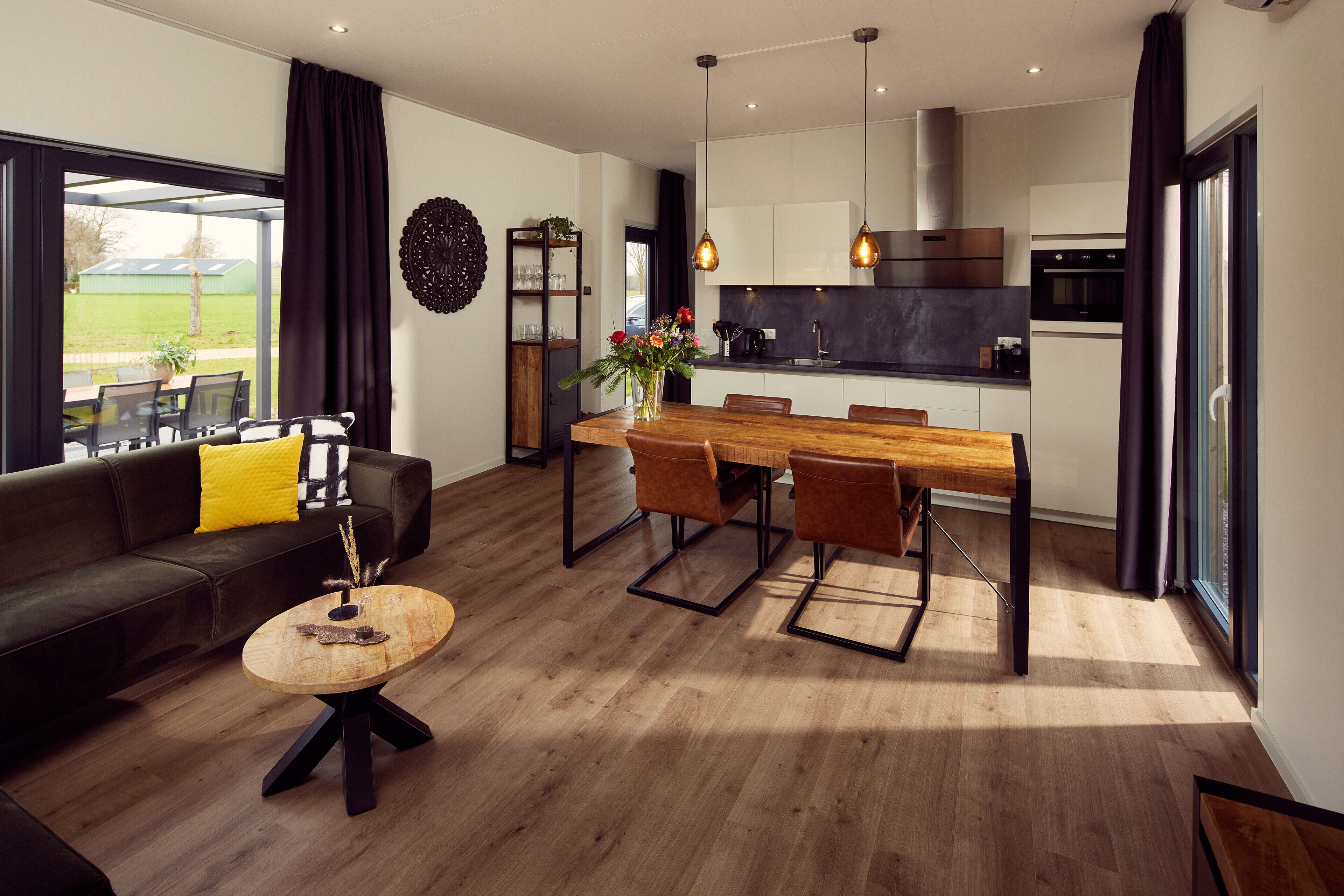 Een moderne keuken met een eethoek, een bank met gele kussens en een houten salontafel.