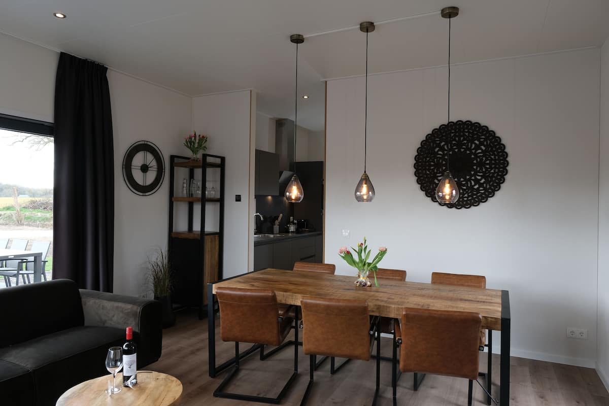 A modern dining area with a wooden table and leather chairs, a black sofa, and a dining table set with a wine bottle and glass.