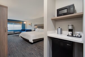 Una habitación de hotel con cama, escritorio, microondas, cafetera y refrigerador pequeño.