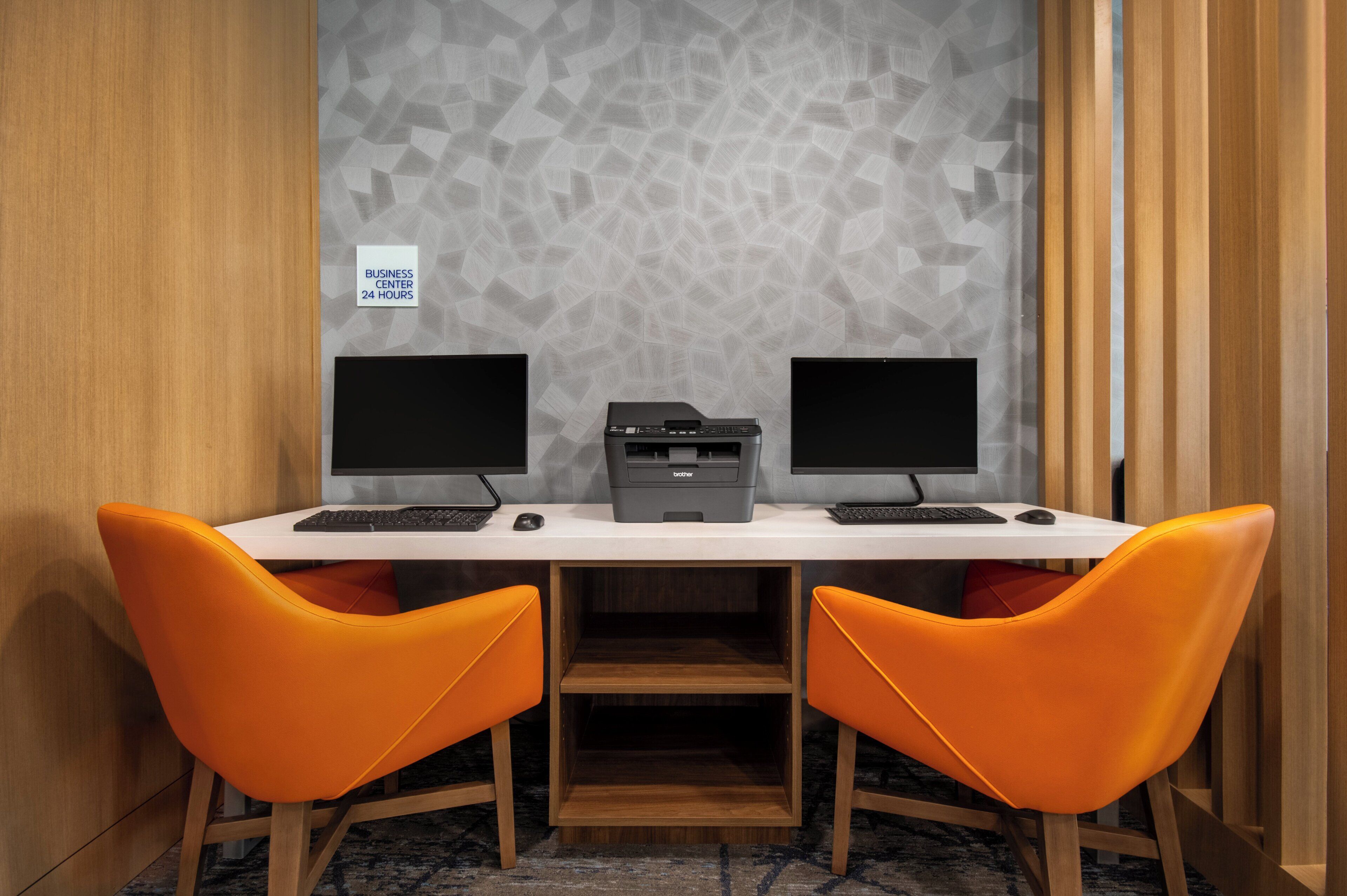 Un espacio de trabajo con dos monitores, una impresora y sillas anaranjadas.