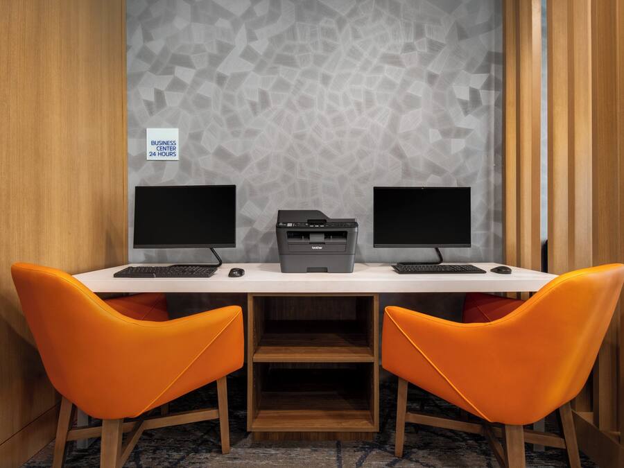 Un espacio de trabajo con dos monitores, una impresora y sillas anaranjadas.
