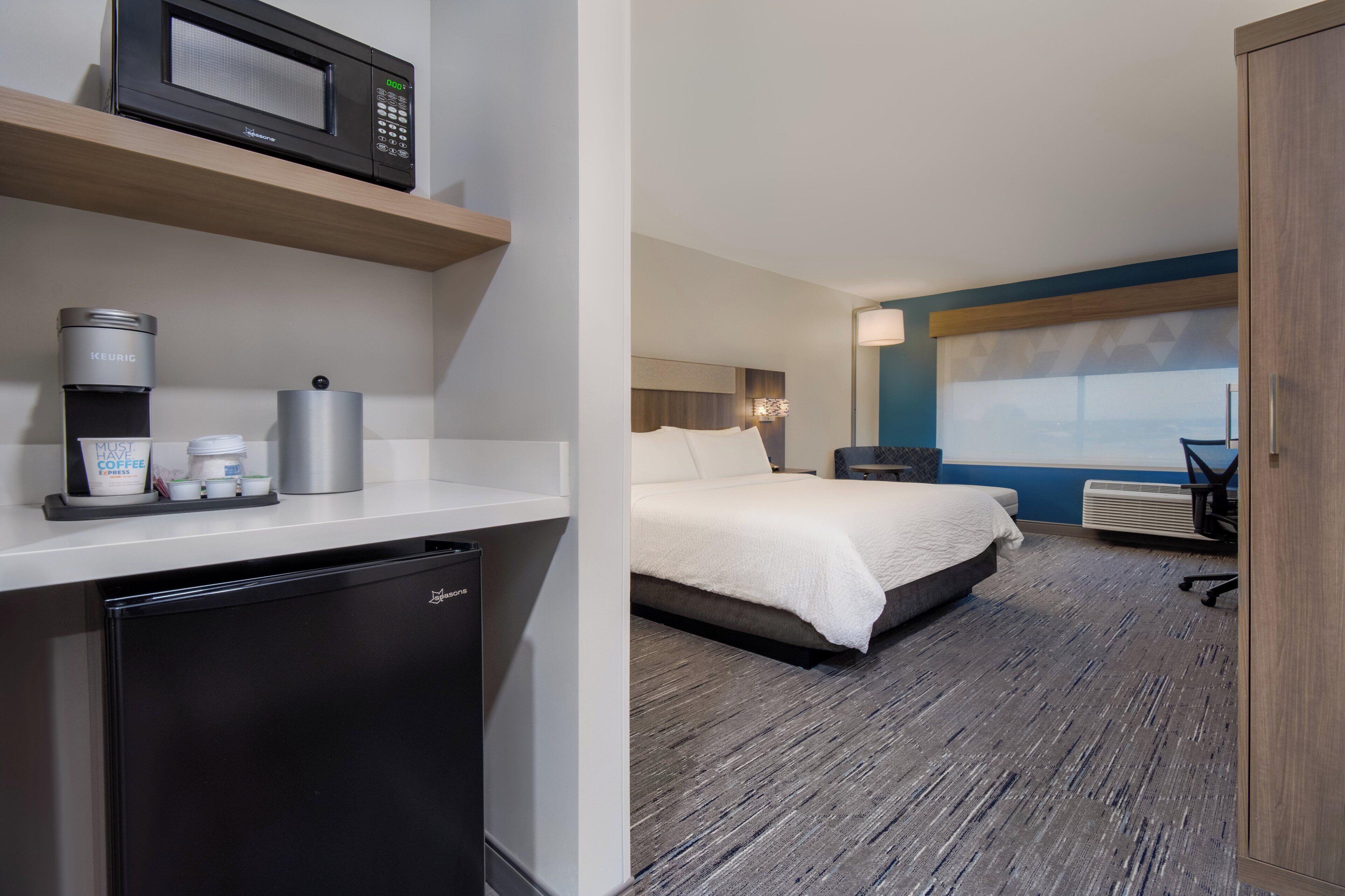 A hotel room with a kitchenette, a bed, a desk, and a view of the city.