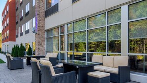 An outdoor patio area with wicker furniture, large windows, and a stone pillar. - Holiday Inn Express & Suites Muskegon - Grand Haven by IHG (Muskegon)