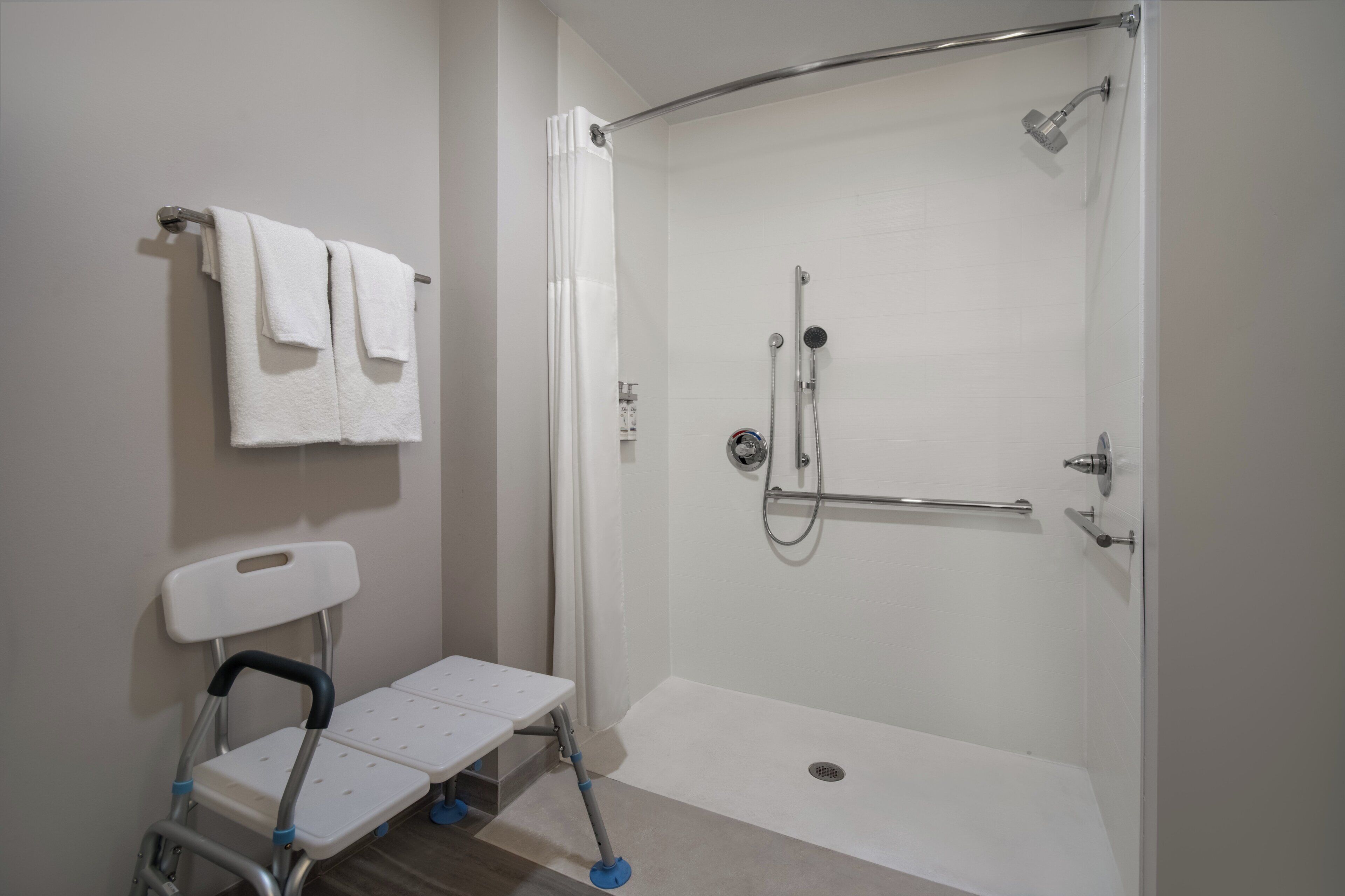 A bathroom with a shower, a white chair, and a towel rack.