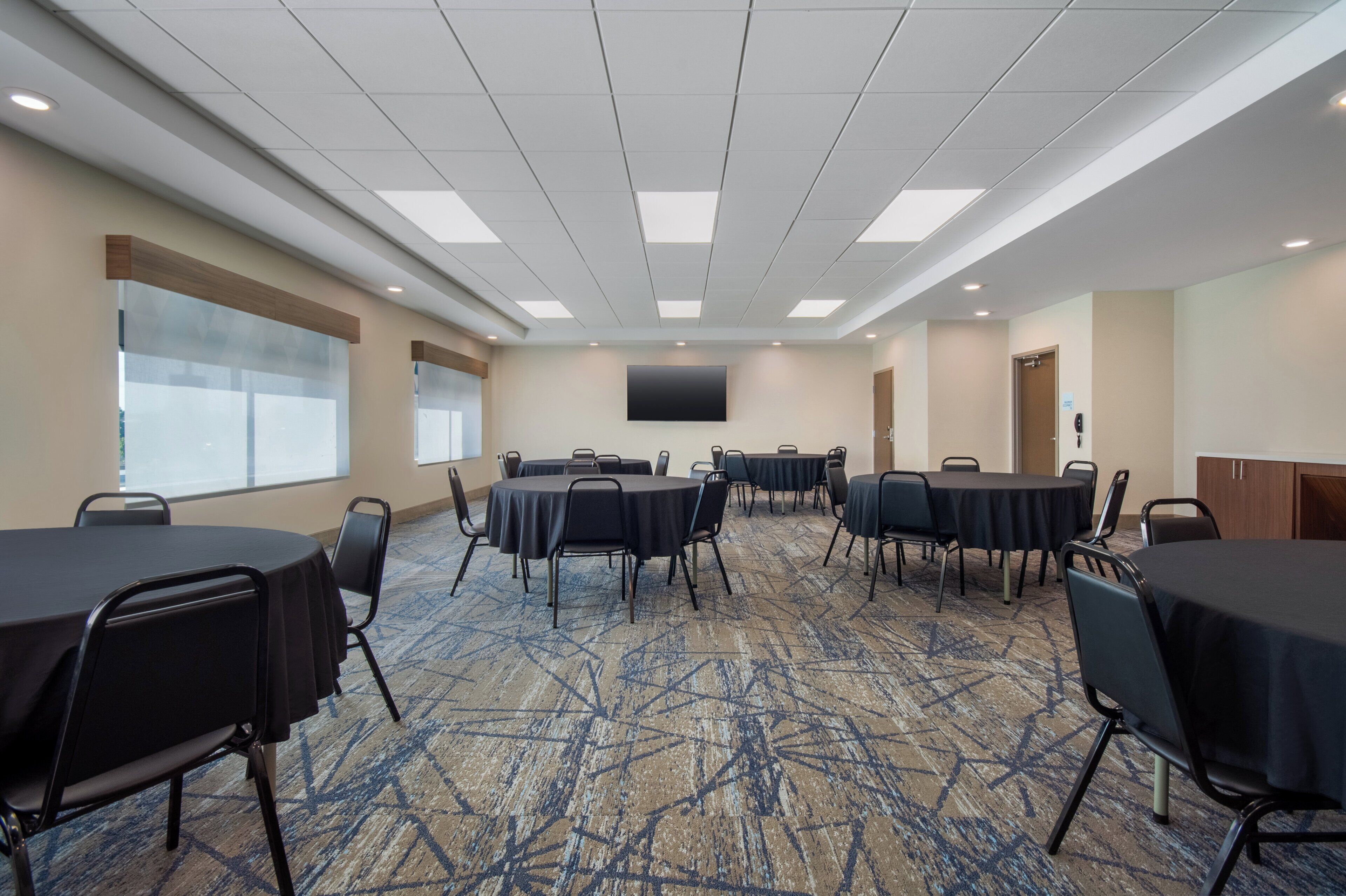 Un salón de conferencias con mesas redondas, sillas, una pantalla grande y piso alfombrado.