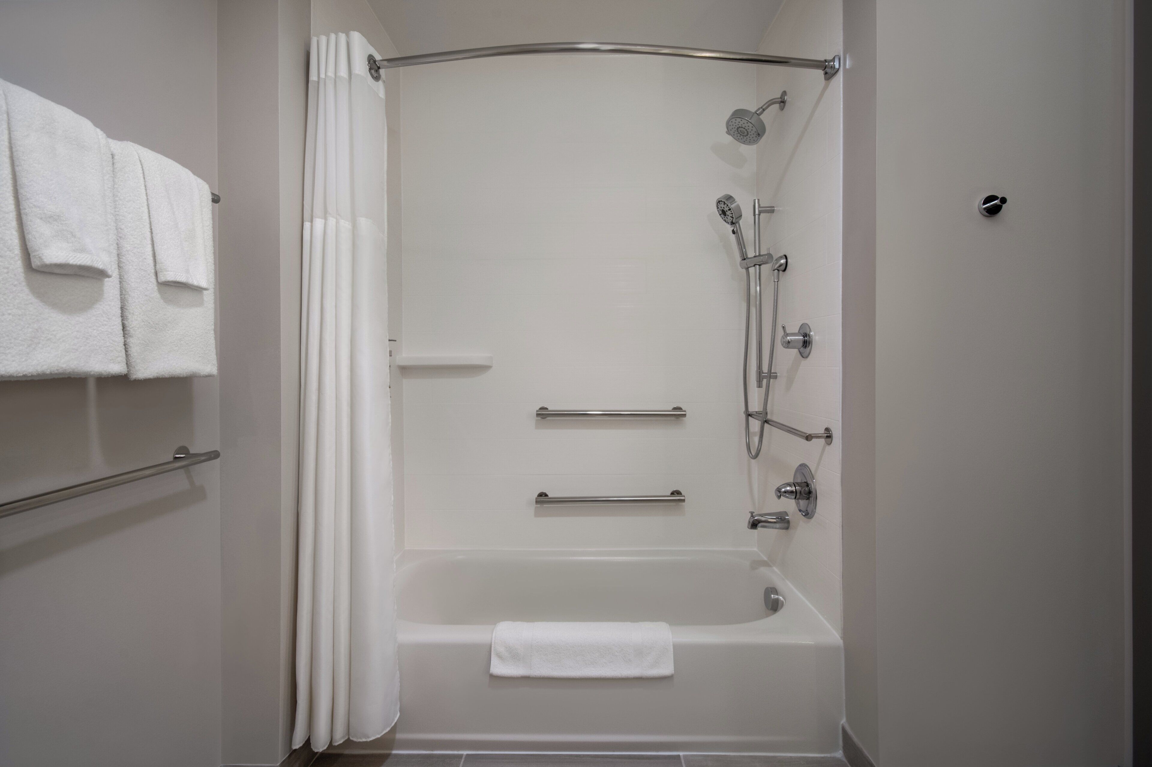 Une salle de bain moderne équipée d’une baignoire, d’une douche et de barres d’appui.