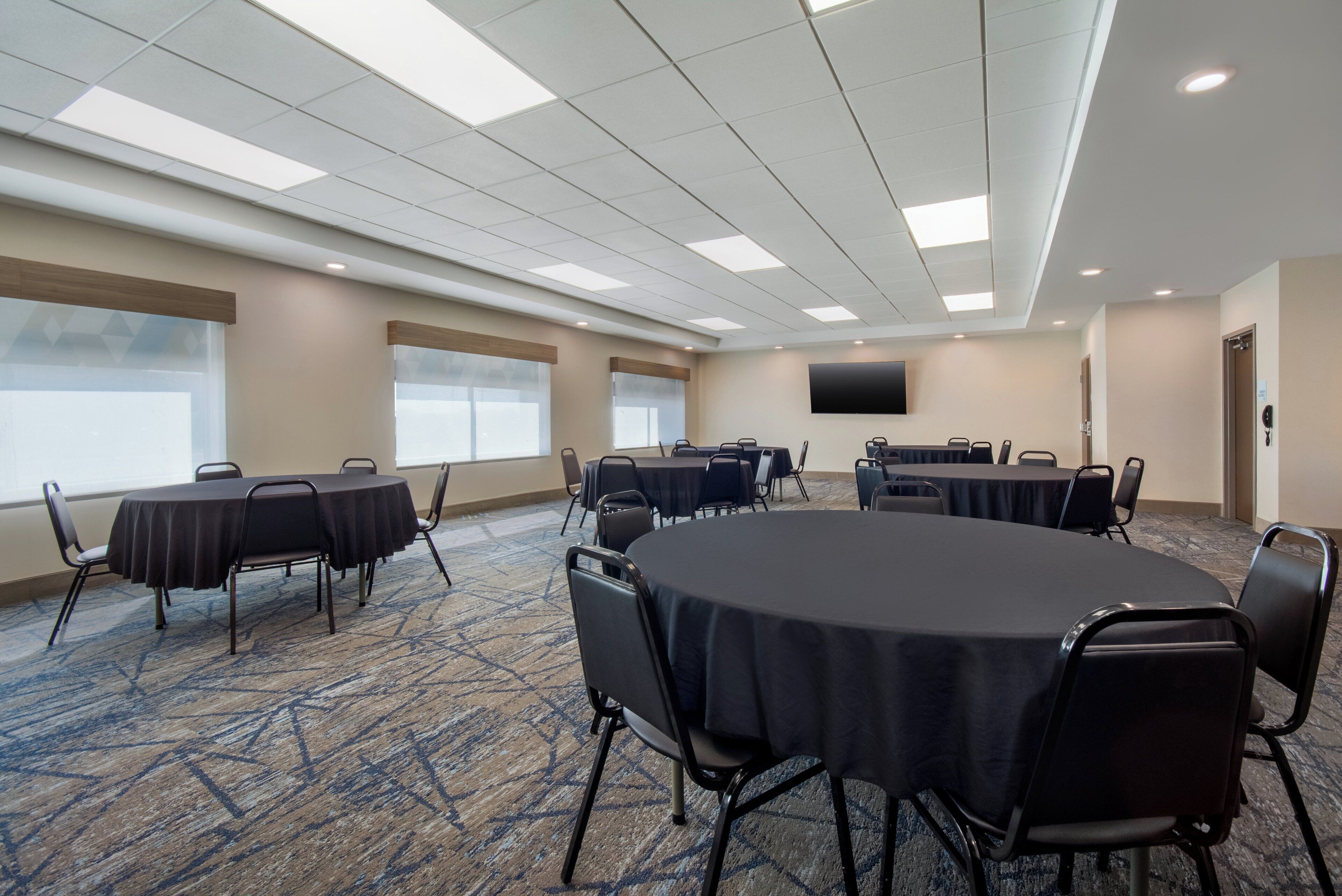 A conference room with round tables, chairs, a flat-screen TV, and large windows.