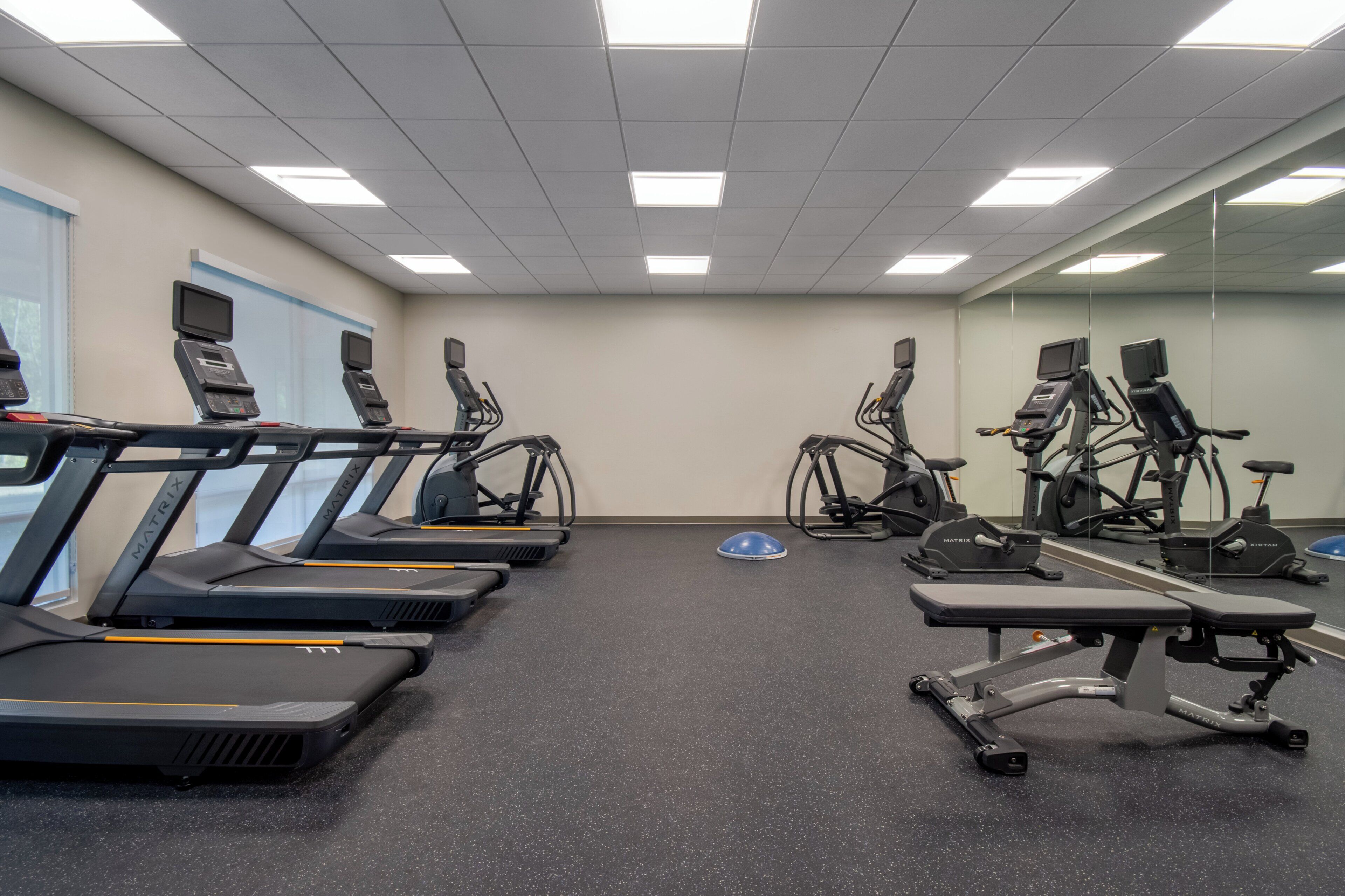 A gym with treadmills, stationary bikes, and a bench.