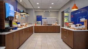 A modern kitchen area with wooden cabinets, a coffee machine, and a bakery display. - Holiday Inn Express & Suites Muskegon - Grand Haven by IHG (Muskegon)