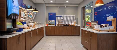A modern kitchen area with wooden cabinets, a coffee machine, and a bakery display.