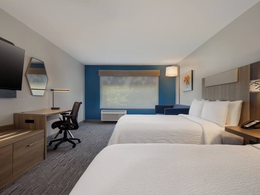 A hotel room with two beds, a desk, a chair, a TV, and a phone on a side table.