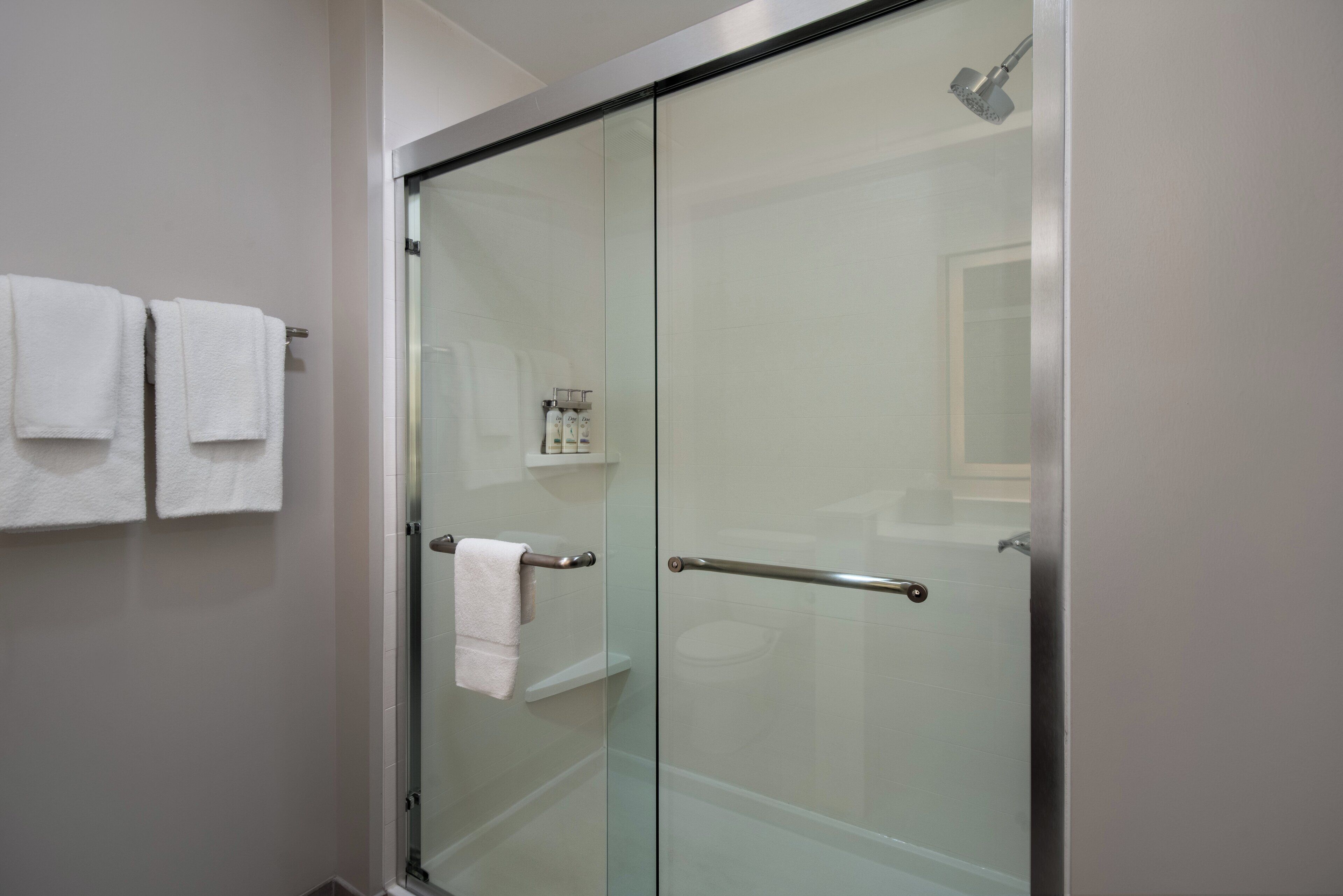 Un baño moderno con cabina de ducha de vidrio, un perchero con dos toallas blancas y una pequeña estantería con artículos de aseo.
